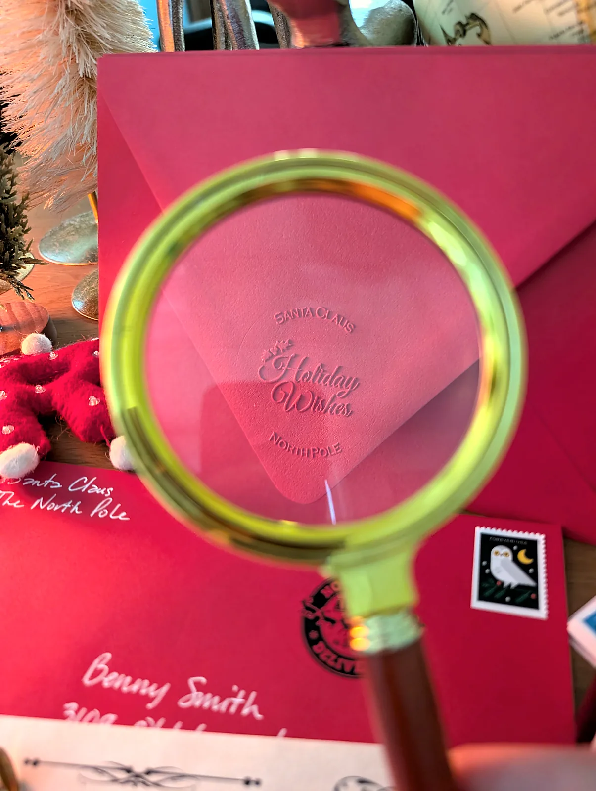 Magnifying glass over the embossed Holiday Wishes seal on the red envelope's flap, the hand-addressed front behind it