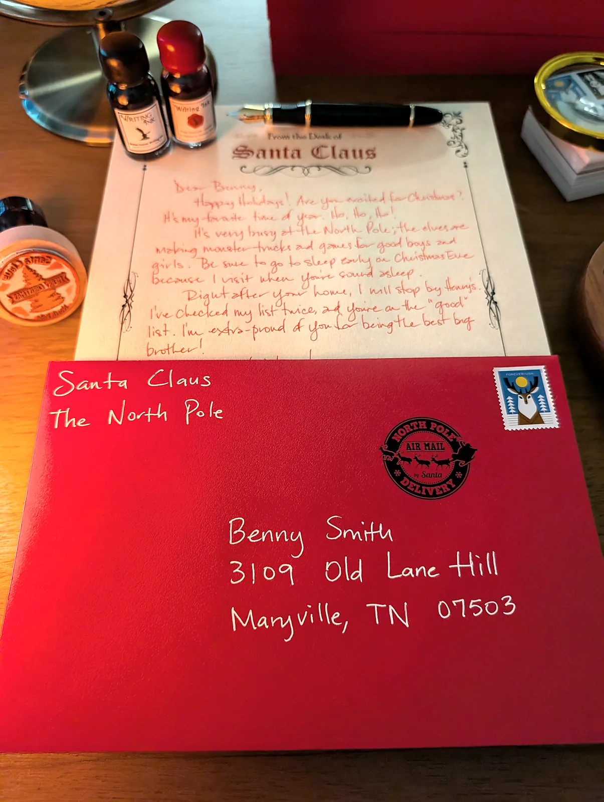 A red Santa envelope hand-addressed in white ink, with the North Pole postmark and a real stamp