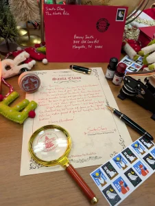 A handwritten Santa letter with the magnifying glass over the North Pole stamp, real stamps and the Merry Christmas garland