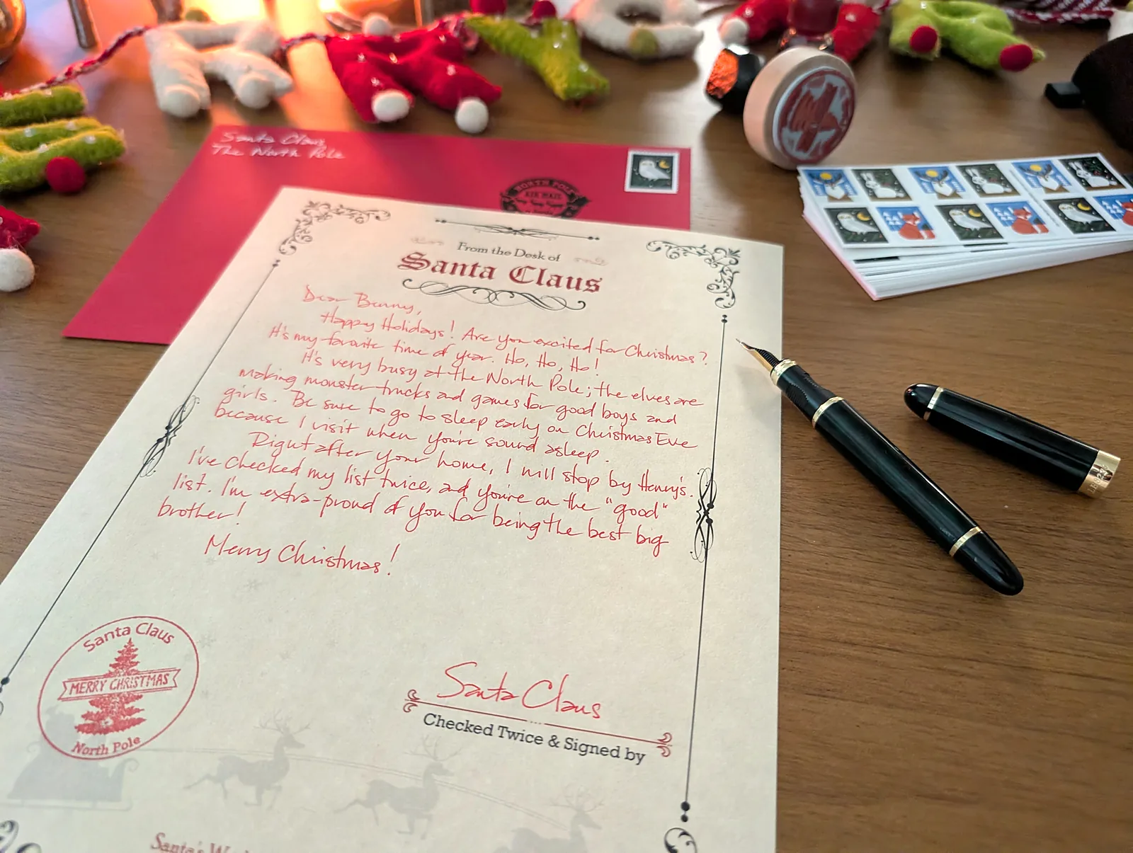 A handwritten Santa letter in red ink under warm light, with red envelopes and stamps