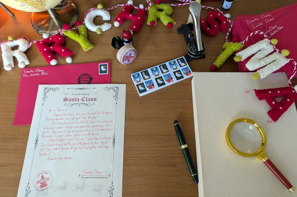 Flat lay of a handwritten Santa letter, red envelope, pen and magnifying glass