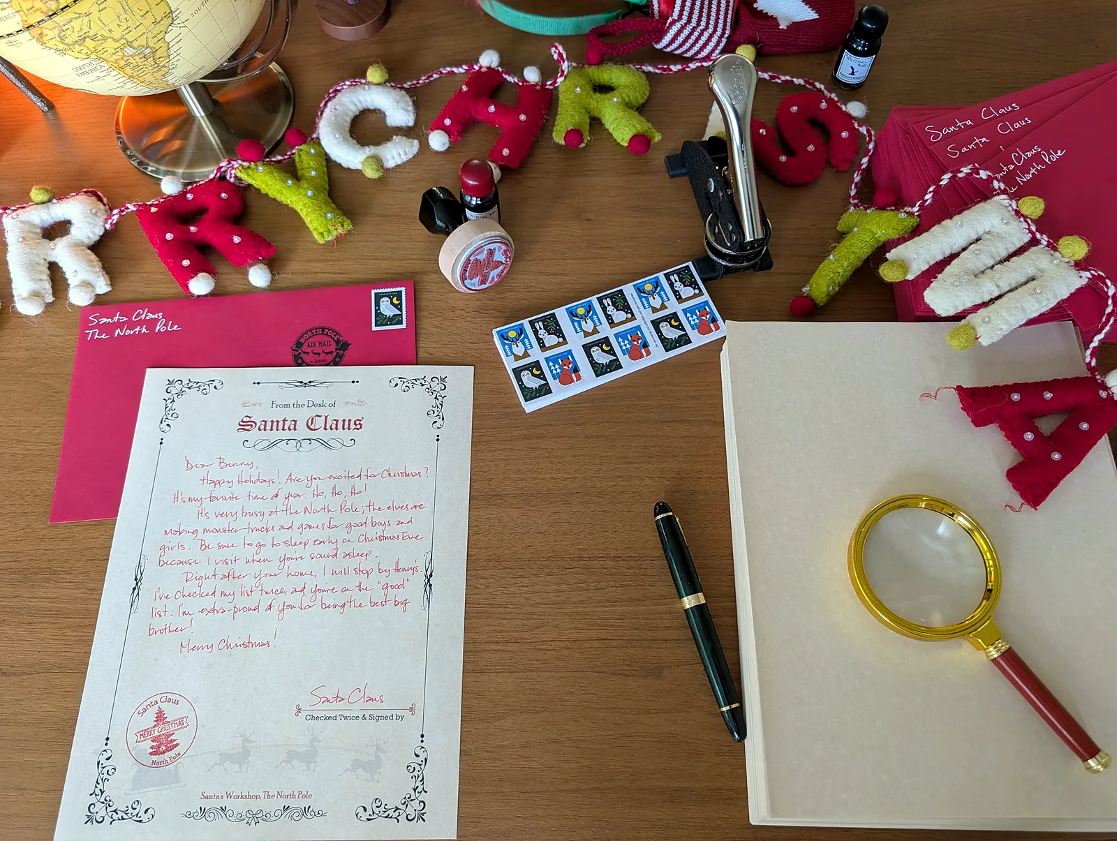 Flat lay of a handwritten Santa letter, red envelope, pen and magnifying glass
