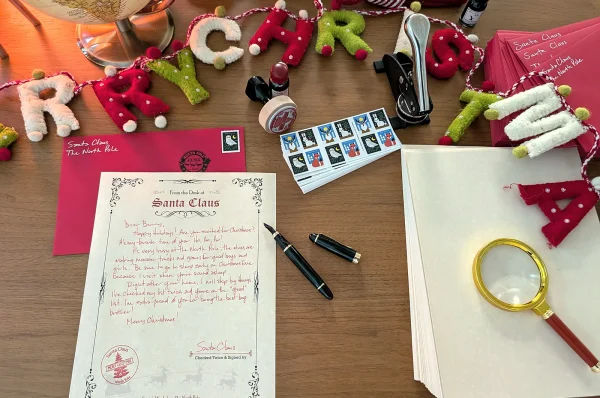Santa letter, red envelope, pen and magnifying glass under a Merry Christmas felt garland