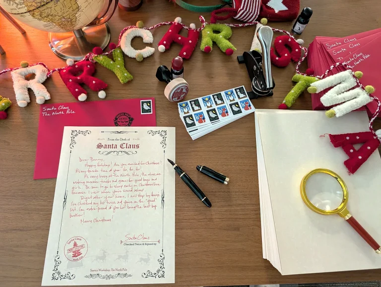 Santa letter, red envelope, pen and magnifying glass under a Merry Christmas felt garland