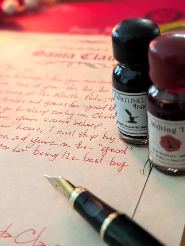 Close-up of red ink handwriting on a Santa letter with the fountain pen nib and ink bottles