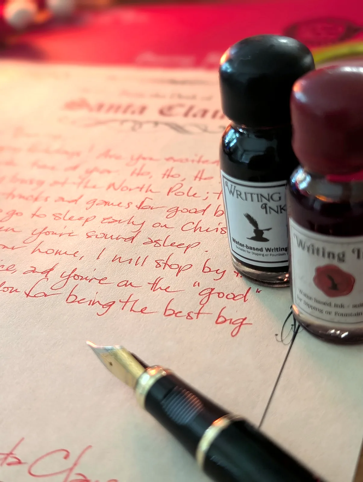 Close-up of red ink handwriting on a letter from Santa, with a fountain pen nib and a bottle of writing ink