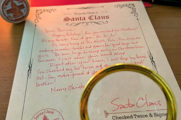Santa's handwritten signature and the red North Pole stamp under a magnifying glass, warm light